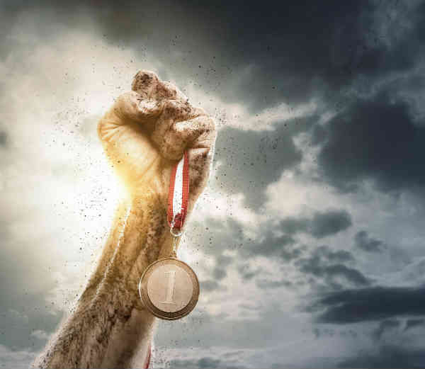 a hand victoriously holding a golden medal